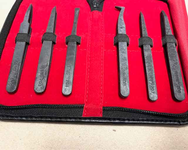 Set of six plastic esd safe tweezers  with black handles in a red case on a beige surface.