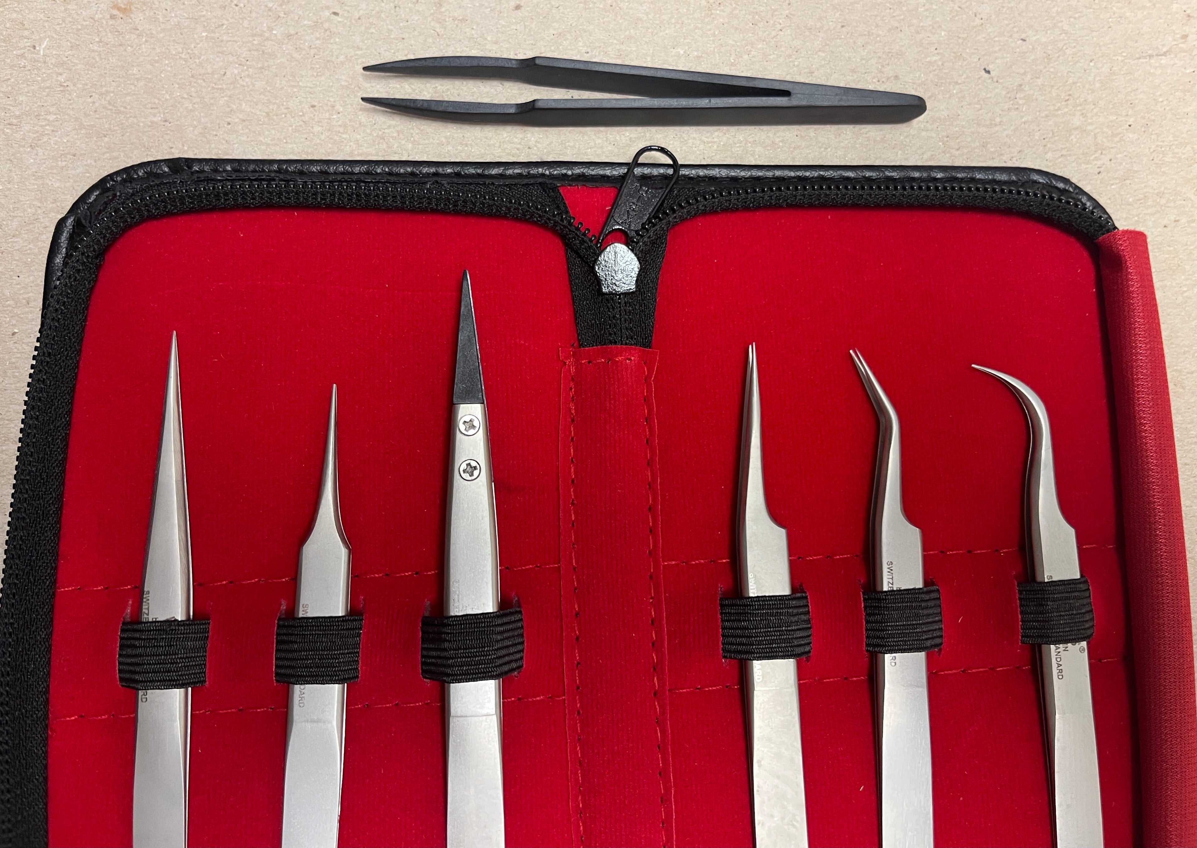 Set of watchmakers tweezers in a red case with black straps on a beige background