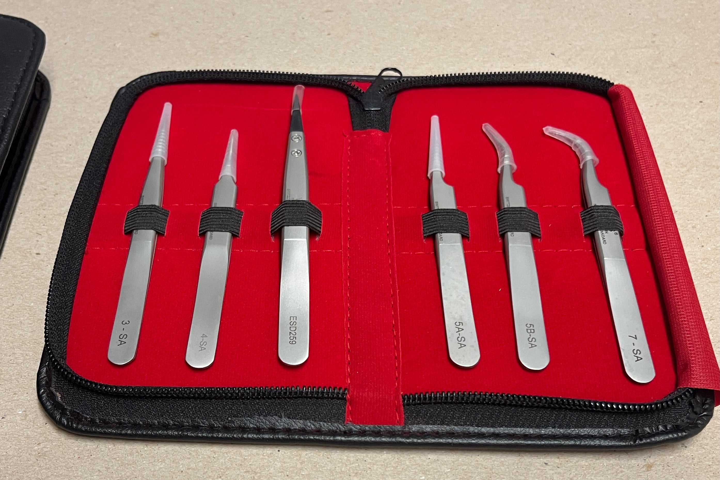 Set of stainless steel tweezers for watchmakers  in a red case on a beige surface